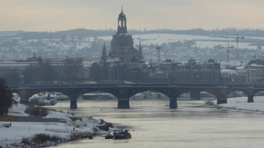 Brücke über Fluss mit verschneiter Stadt im Hintergrund.
