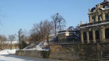 Historic building beside snowy riverbank, clear sky.