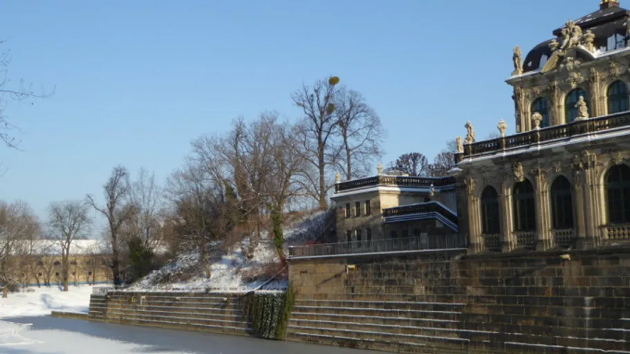 Historisches Gebäude neben verschneitem Flussufer, klarer Himmel.