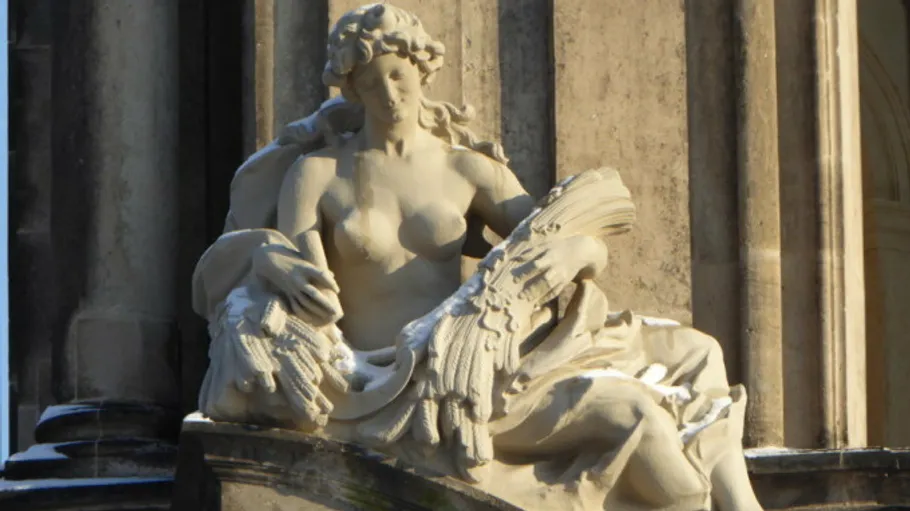 Steinskulptur einer sitzenden Frau vor Gebäude.