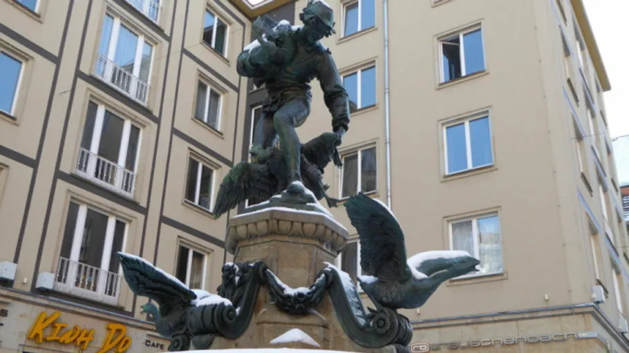 Statue eines Mannes mit Vögeln in städtischer Umgebung.