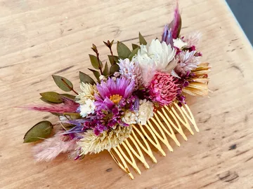 Haarkamm mit bunten Trockenblumen dekoriert auf Holzuntergrund.