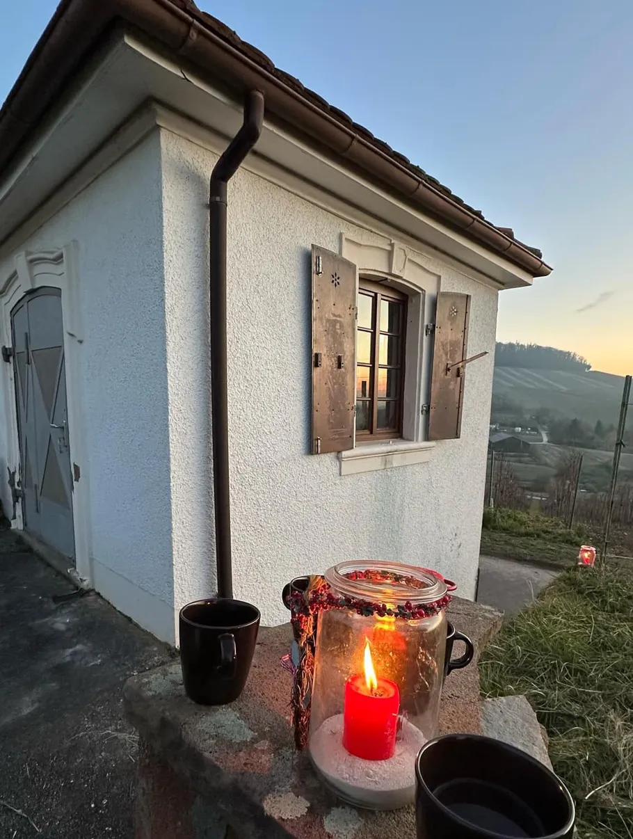 Candle in jar beside small house at sunset.