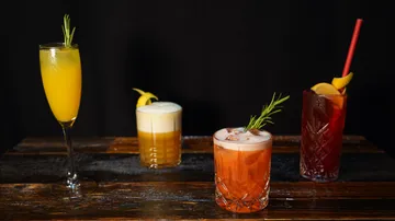 Four cocktails on wooden table, garnished elegantly.