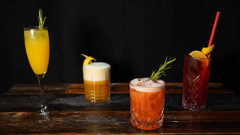 Vier Cocktails auf Holztisch, elegant garniert.