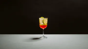 Cocktailglas mit Limette auf grauer Fläche.