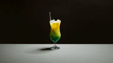 Bunter Cocktail mit Strohhalm auf dunklem Hintergrund.