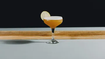 Cocktail mit Limettengarnitur auf Tisch.