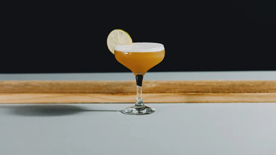 Cocktail with lime garnish on table.