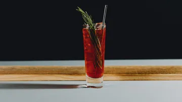 Red cocktail with rosemary on wooden table.