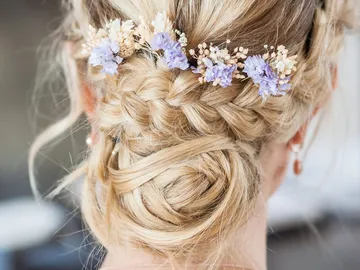 Gestylte Haare mit Blumenarrangement, elegant im Hintergrund.