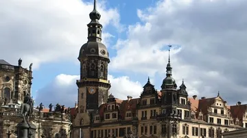 Historic buildings and tower under cloudy sky.