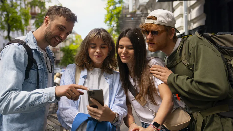 Vier Freunde schauen im Freien auf ein Handy.
