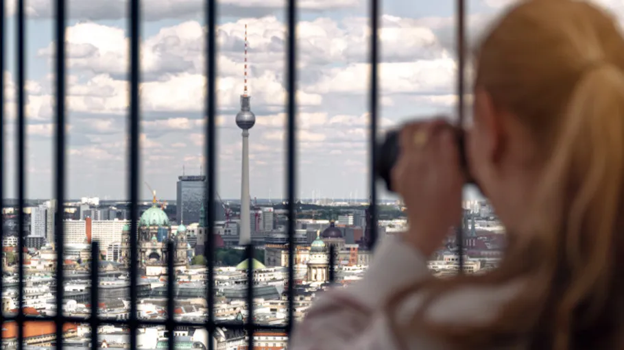 Frau fotografiert Berliner Skyline durch Gitterstäbe.