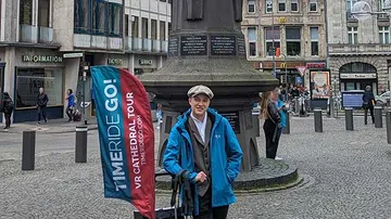 Person standing in plaza next to statue and banner.