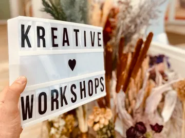 Kreatives Schild zeigt Workshops auf einem Blumenarrangement.