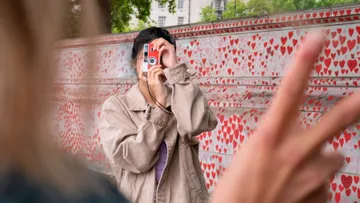 Person taking photo with a heart-patterned wall backdrop.