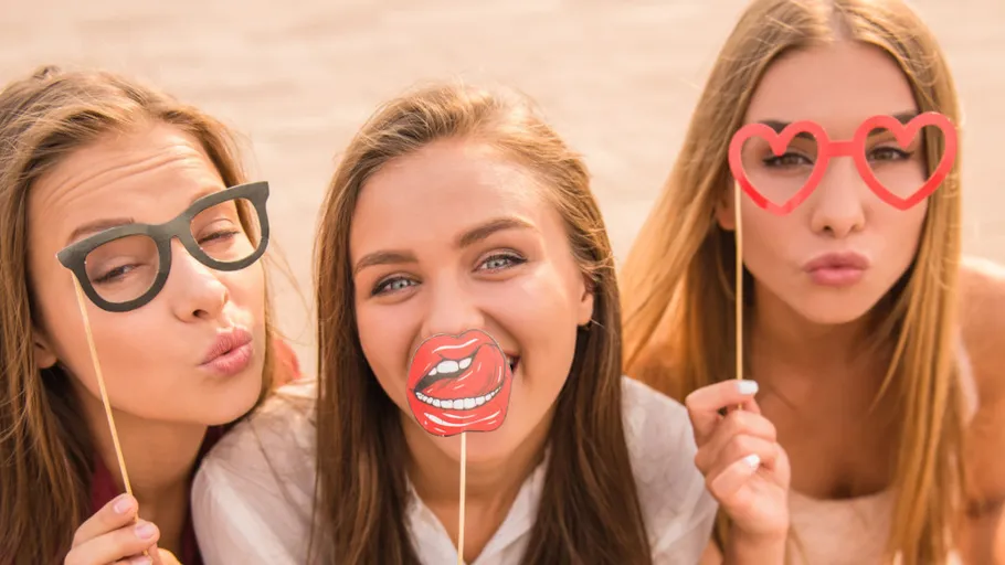 Frauen posieren mit lustigen Foto-Requisiten im Freien.