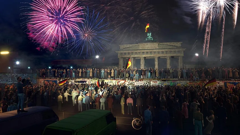 Menschenmenge feiert an der Berliner Mauer mit Feuerwerk.