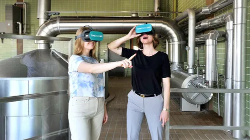 Two women using VR headsets in an industrial setting.