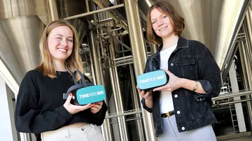Two women holding VR headsets, industrial background.