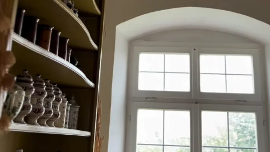 Regale mit Gläsern neben gewölbtem Fenster.