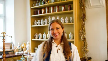 Woman smiling in historical pharmacy setting.
