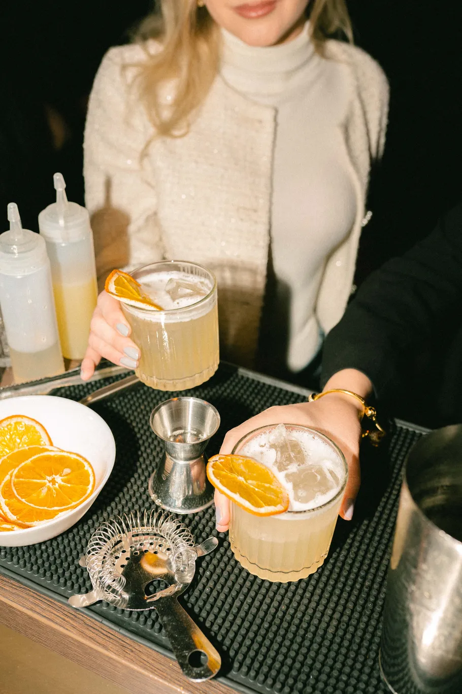 Zwei Personen halten Cocktails mit Orangenscheiben.