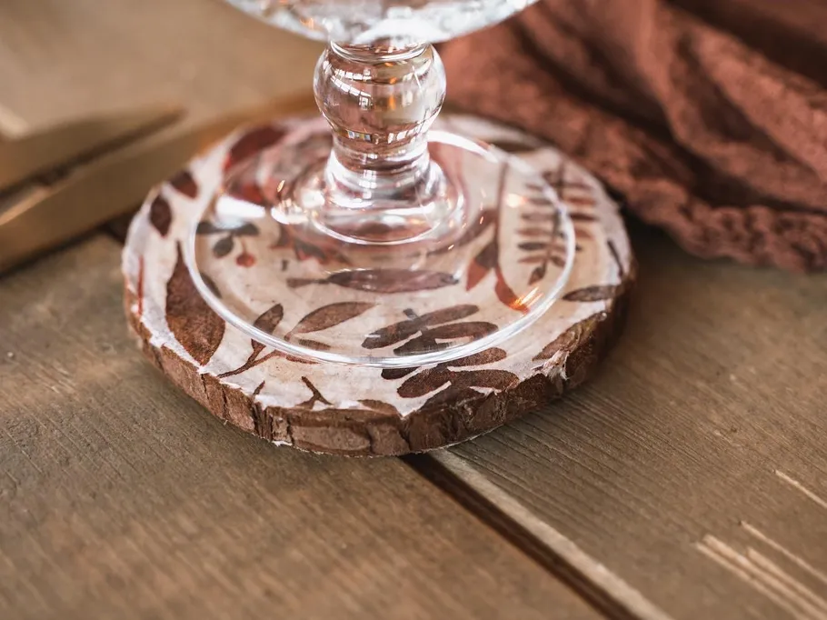 A glass is placed on a decorative wooden trivet.