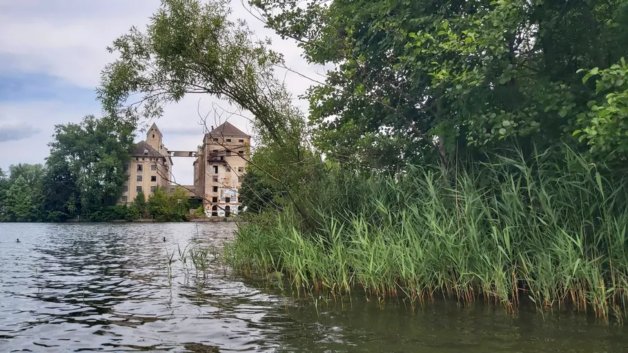 Abandoned building beside a lake surrounded by trees.