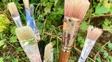Paintbrushes with paint in a garden setting.