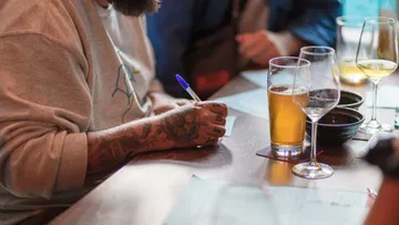 Person schreibt auf Papier neben Biergläsern.