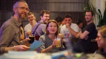 Personen sitzen, reden und trinken in einer Bar.