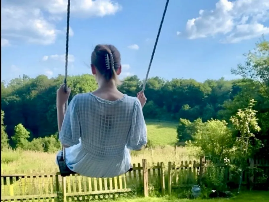 Person schaukelt im sonnigen Garten, Felder hinten.