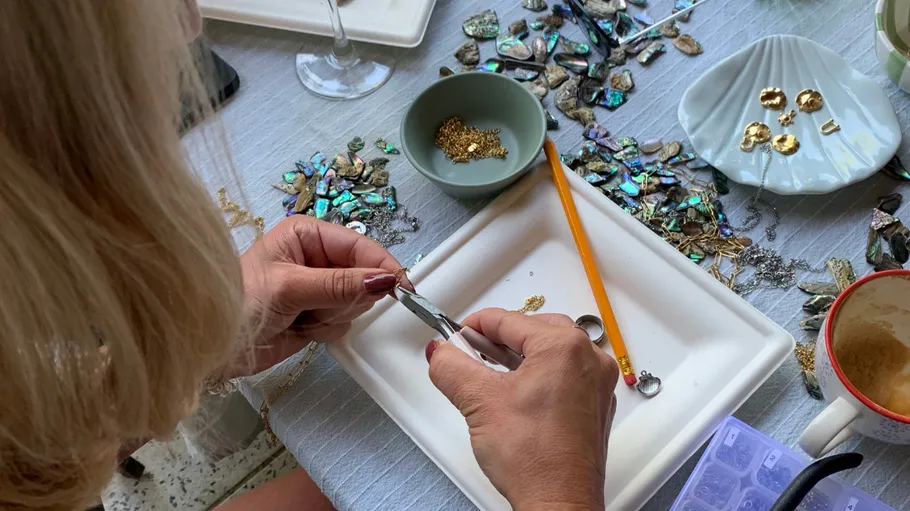 Person fertigt Schmuck an einem Tisch.