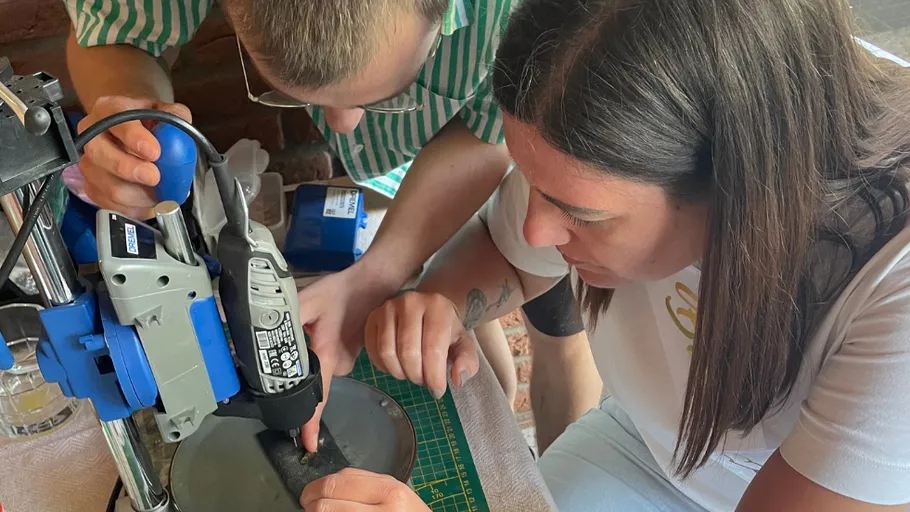 Two people using a drill press at a table.
