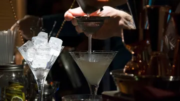 Bartender pours cocktail through strainer into glass.