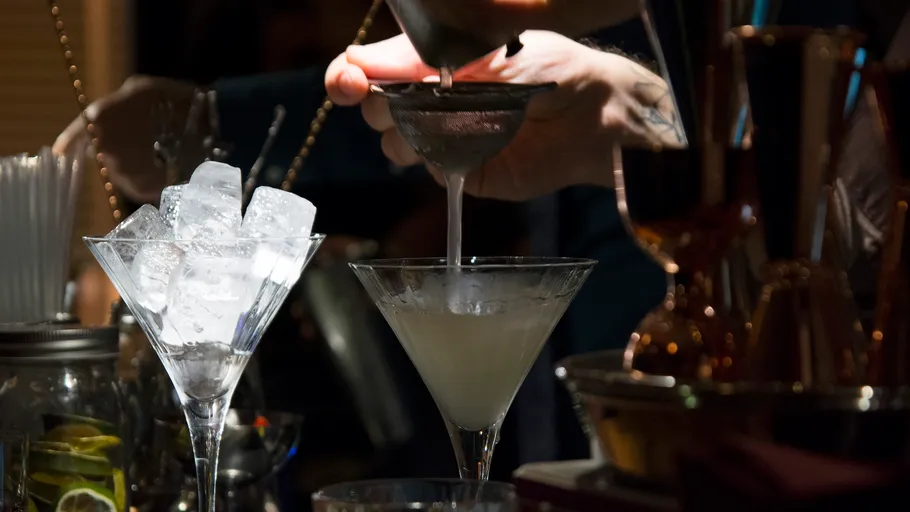 Barkeeper gießt Cocktail durch Sieb ins Glas.