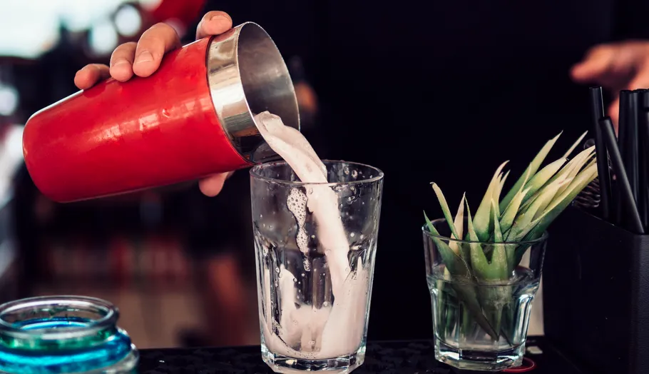 Barkeeper gießt Getränk ins Glas, dekorierter Tresen.