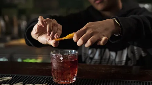 Bartender garnishes cocktail with orange peel at bar.
