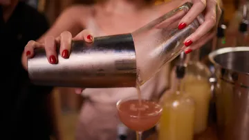 Bartender pouring cocktail with metal shaker.
