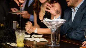 Bartender mixing drink for people at bar.