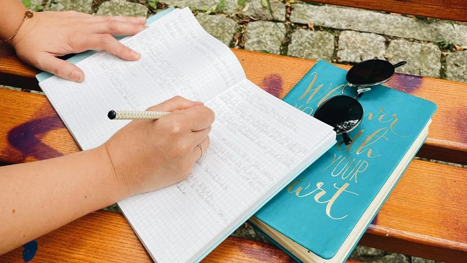 Person writing in notebook on park bench.