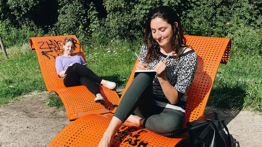 Zwei Frauen entspannen auf orangefarbenen Liegen im Park.