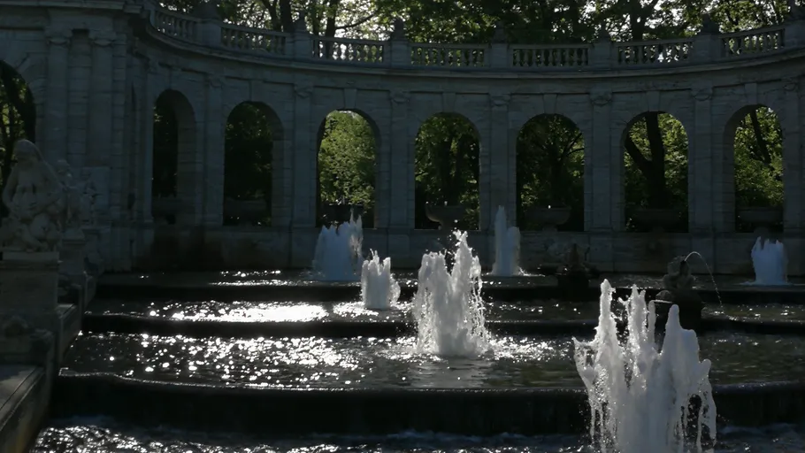 Fountain with arched stone wall, sunny day.