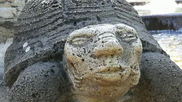 Steinschildkrötenskulptur mit menschlichem Gesicht.