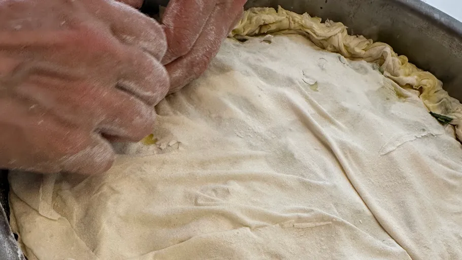 Hands shaping dough in metal baking tray.