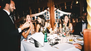 Menschen lachen bei einem Abendessen drinnen.