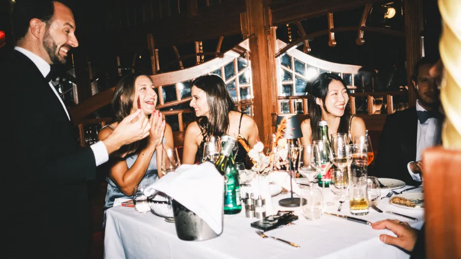 Menschen lachen bei einem Abendessen drinnen.
