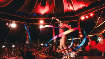 Performer in red with ribbons on stage under tent.